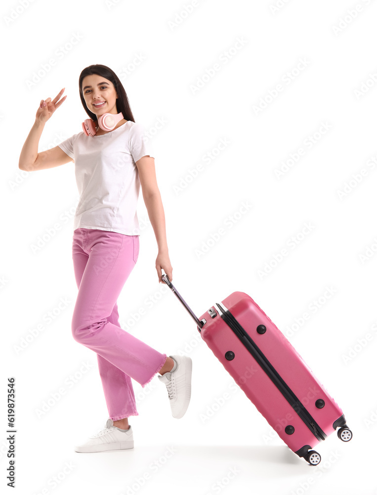 Young woman with pink suitcase showing victory gesture on white background