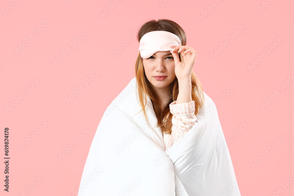 Young woman with sleeping mask and blanket on pink background