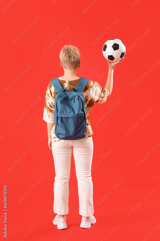 Female student with backpack and soccer ball on red background, back view