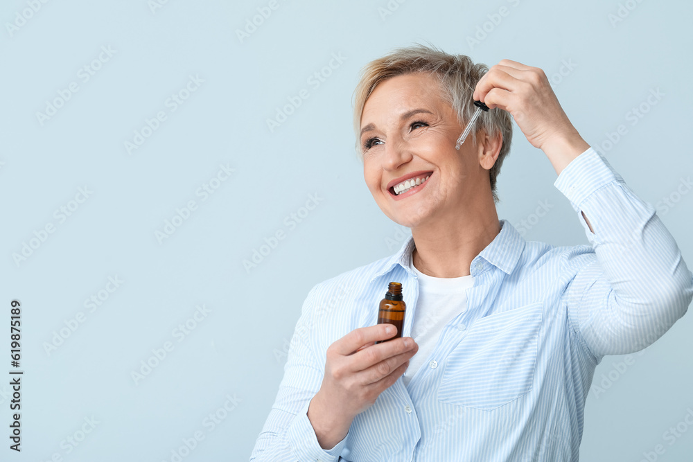 Mature woman applying serum on light background