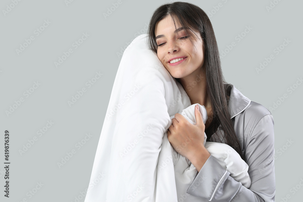 Beautiful happy young woman with soft blanket sleeping on grey background