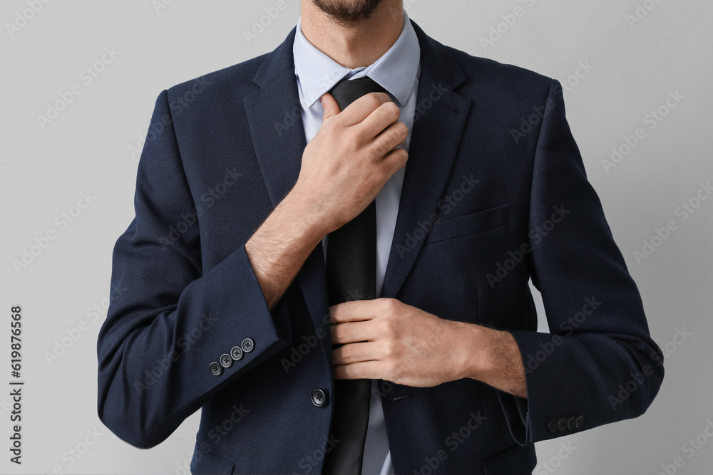 Young businessman in suit fixing necktie on light background, closeup