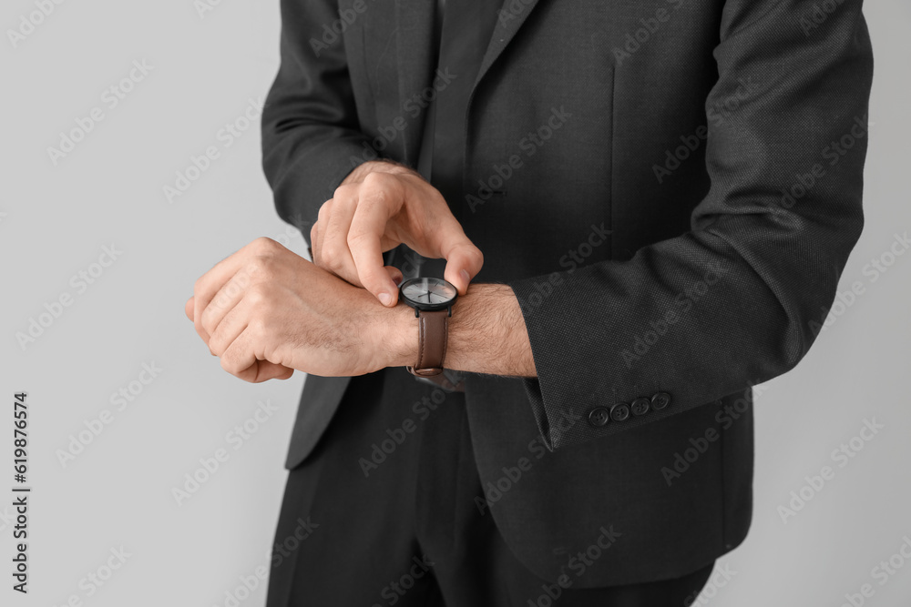 Young businessman in suit looking at wristwatch on light background, closeup