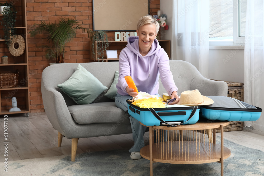 Mature woman with sunscreen packing suitcase at home