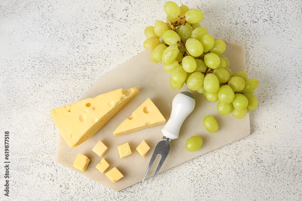 Board with tasty Swiss cheese and grapes on light background