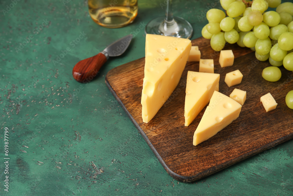 Wooden board with tasty Swiss cheese on green background