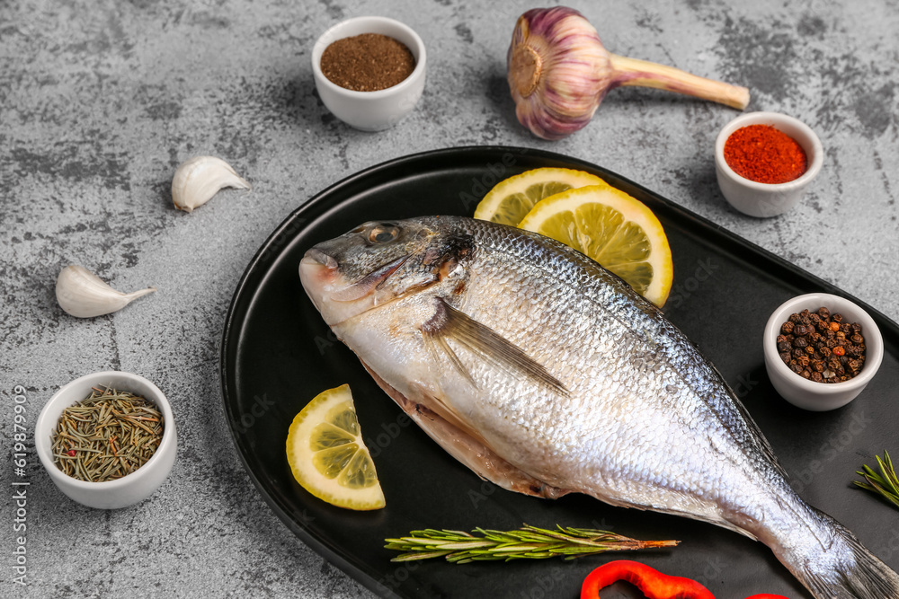 Tray of raw dorado fish with lemon and spices on light background