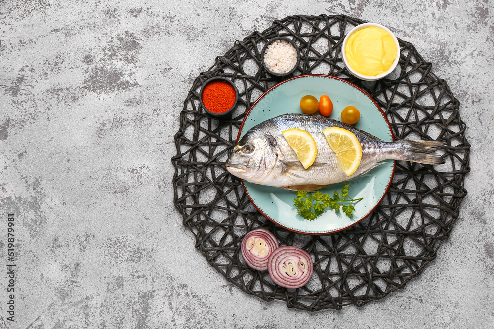 Plate of raw dorado fish with lemon and tomatoes on light background