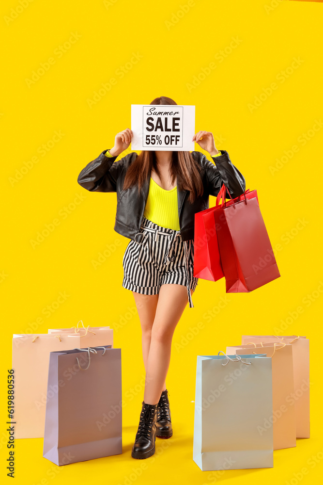 Young woman holding paper with text SUMMER SALE and shopping bags on yellow background