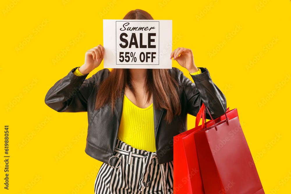 Young woman holding paper with text SUMMER SALE and shopping bags on yellow background