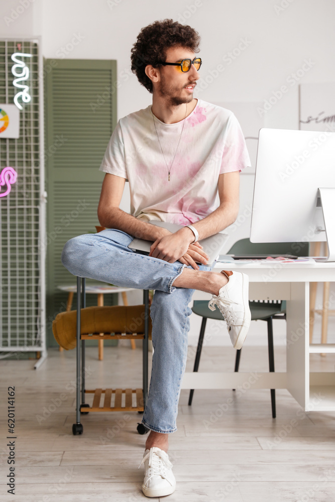 Male graphic designer with laptop sitting in office