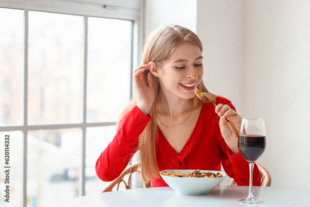 Young woman with glass of wine eating tasty pasta in restaurant