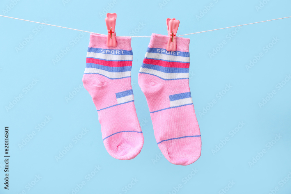 Pair of socks hanging on rope against color background