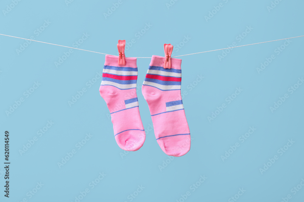 Pair of socks hanging on rope against color background