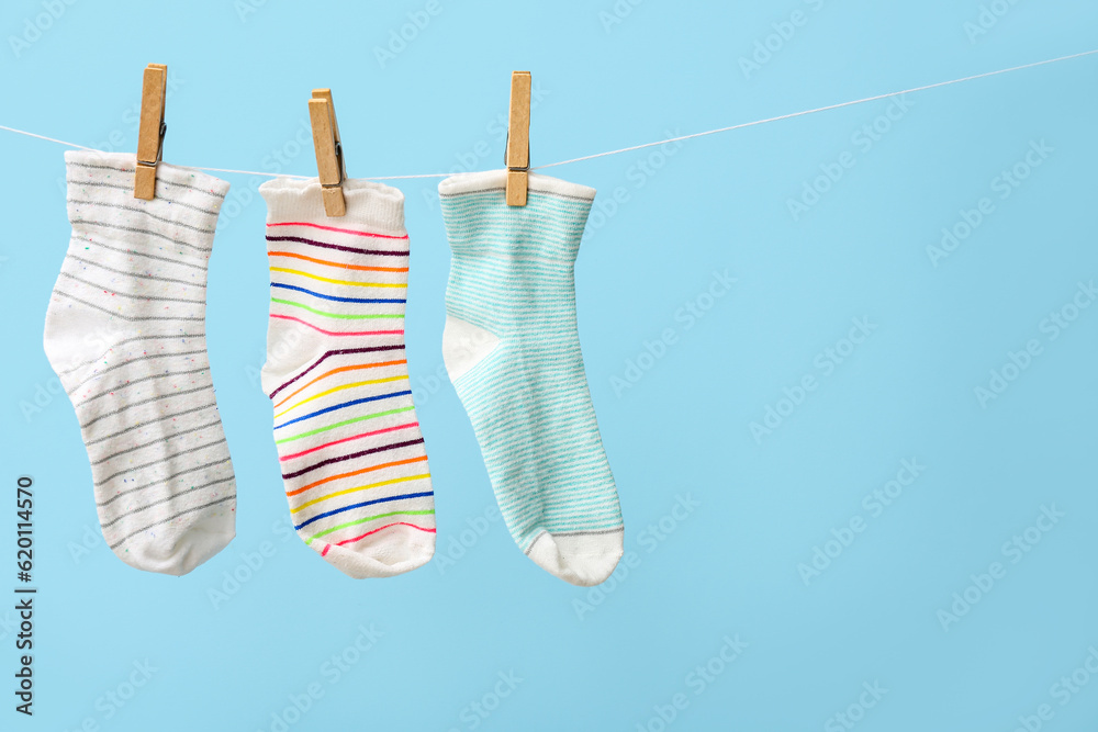 Different socks hanging on rope against color background