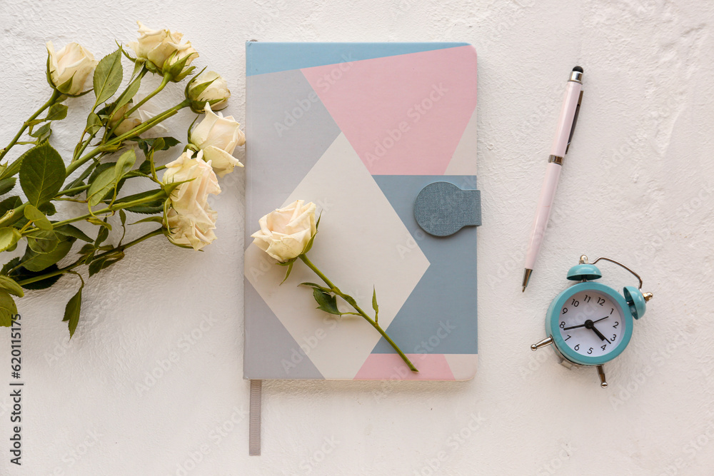 Composition with notebook, pen, alarm clock and beautiful rose flowers on light background