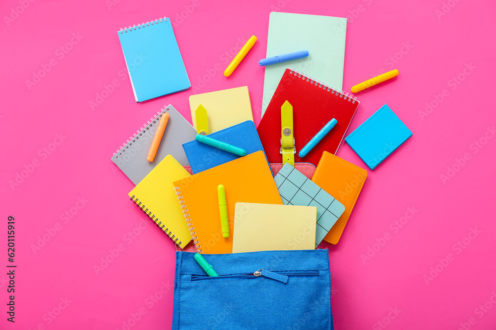 Blue school backpack with notebooks and markers on pink background