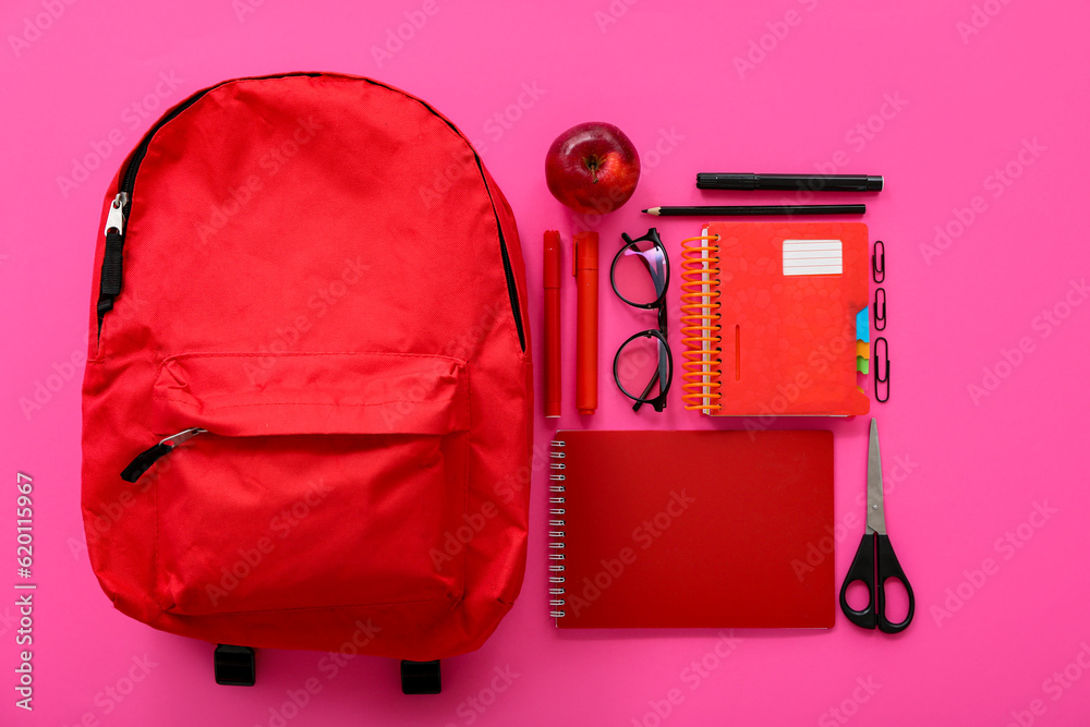 Red school backpack with notebooks, eyeglasses and apple on pink background