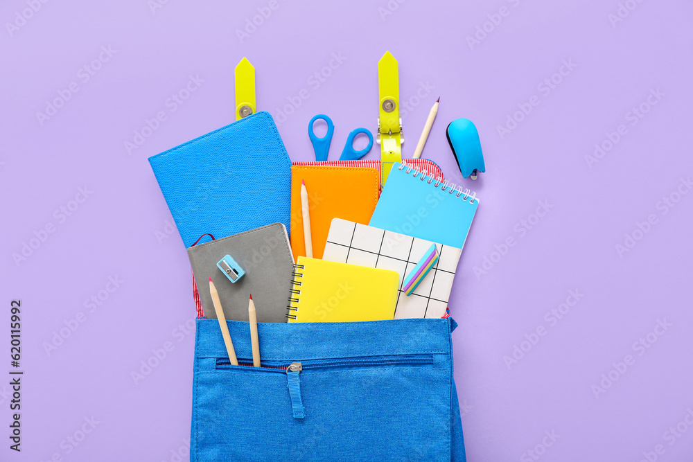 Blue school backpack with notebooks, color pencils and scissors on lilac background