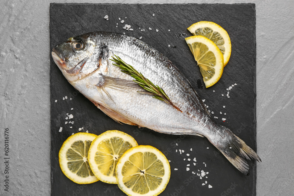 Slate board of raw dorado fish with lemon on grey background