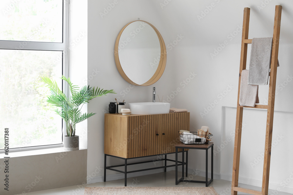 Sink bowl and bath accessories on wooden cabinet in interior of light bathroom