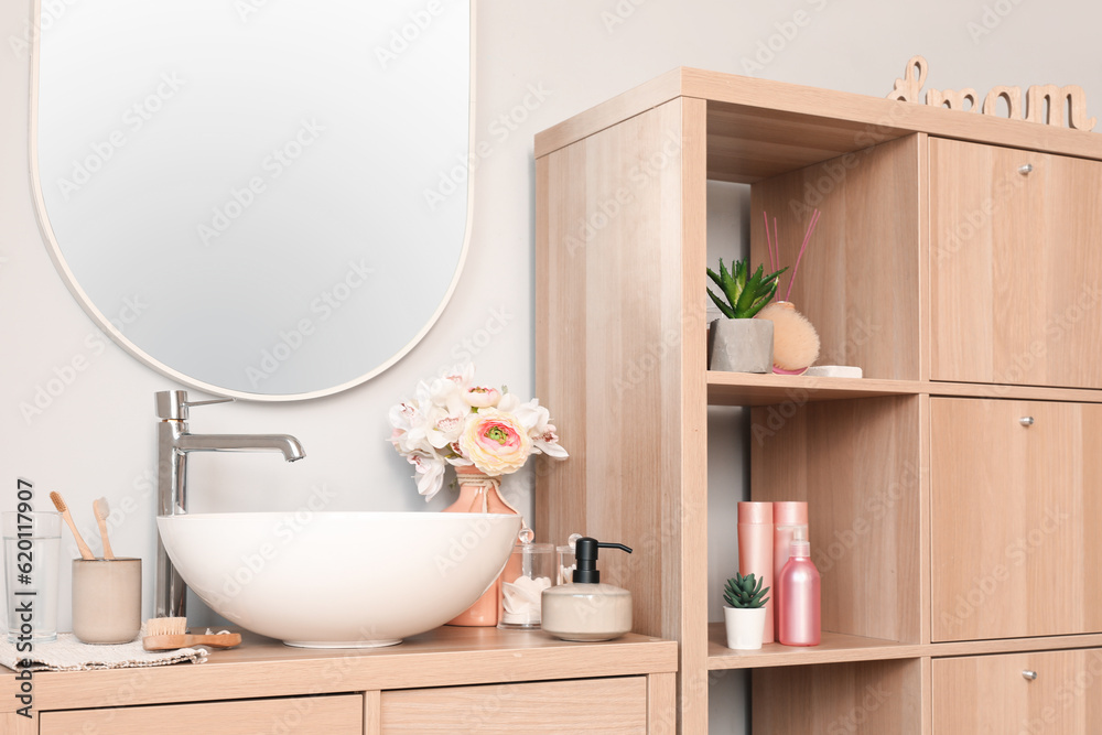 Interior of light bathroom with sink bowl, bath accessories and ranunculus flowers