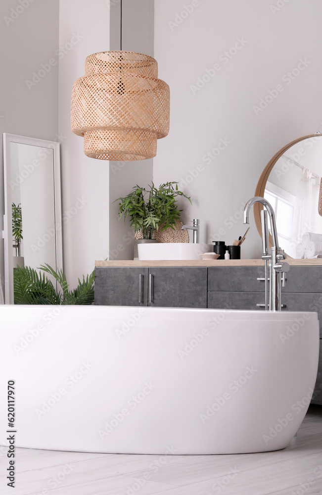 Interior of light bathroom with bathtub, sink bowl and bath accessories on grey counters