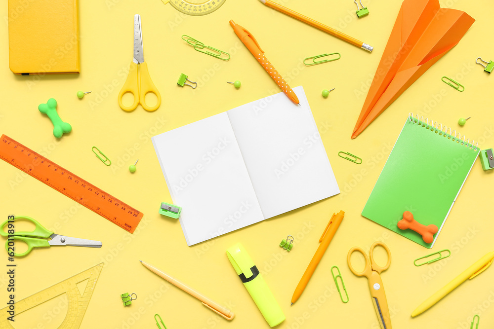 Composition with blank notebook and different school stationery on yellow background