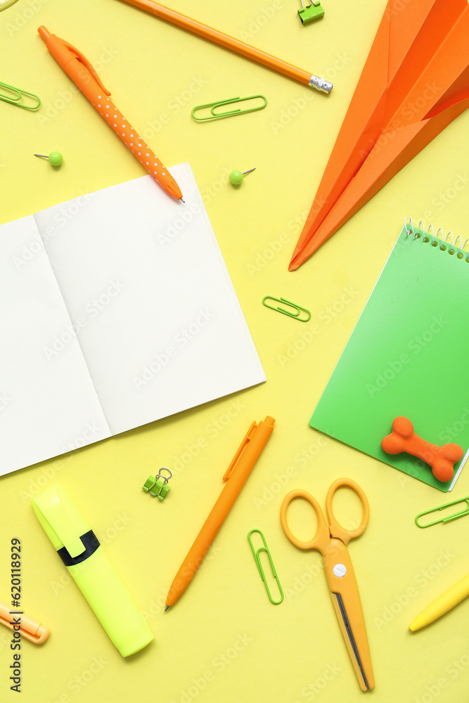 Composition with blank notebook and different school stationery on yellow background