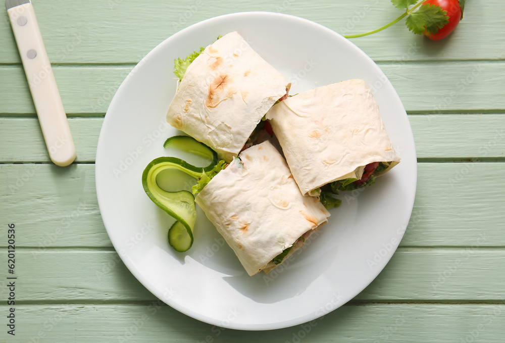 Plate of tasty lavash rolls with tomatoes and greens on green wooden background