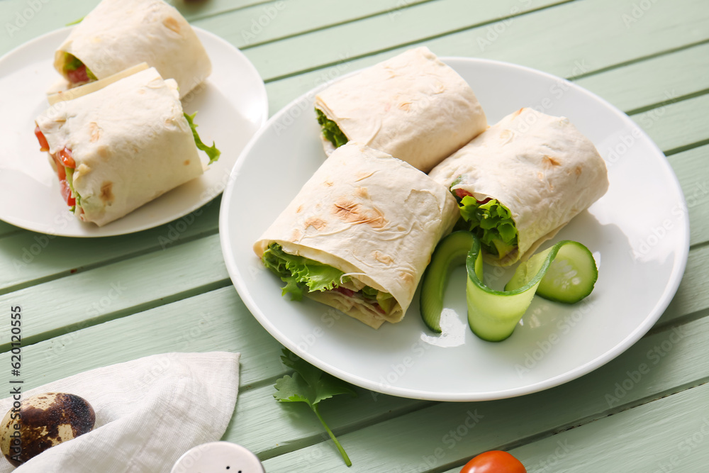 Plates of tasty lavash rolls with tomatoes and greens on green wooden background