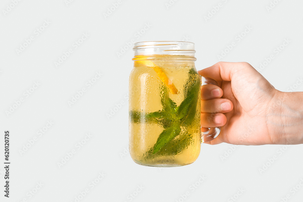 Female hand holding mason jar of ice tea with lemon and mint on white background