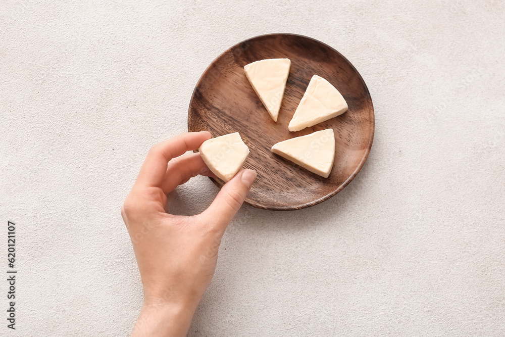 Woman eating triangle of tasty processed cheese on light background