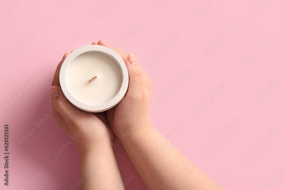 Female hands holding candle on pink background