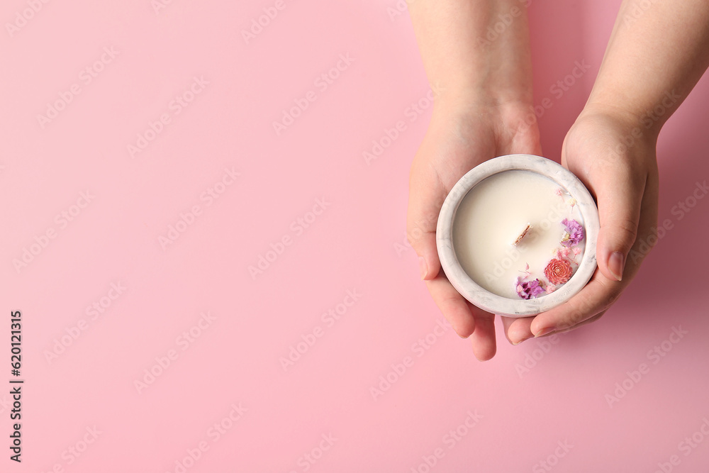 Female hands holding candle with flowers on pink background