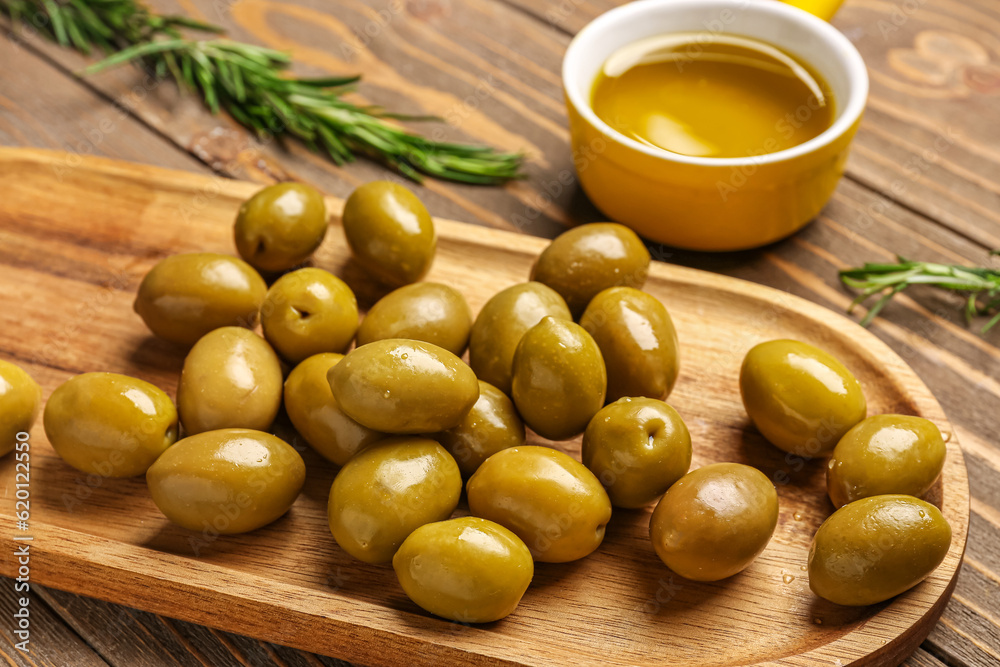 Board with ripe olives on wooden background