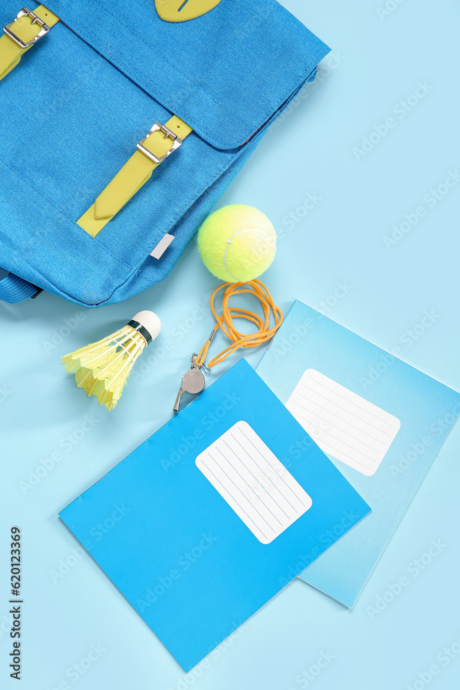 Backpack with tennis ball, whistle, badminton shuttlecock and notebooks on blue background