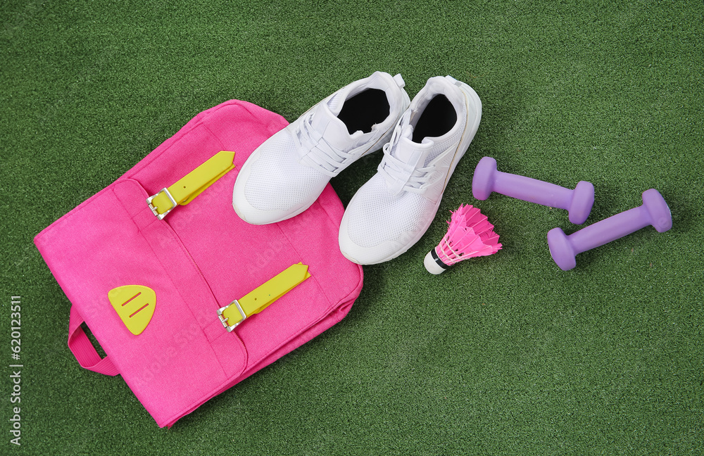 Backpack with sneakers, badminton shuttlecock and dumbbells on color background