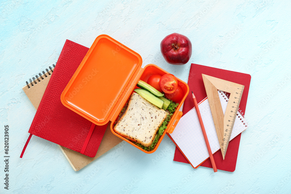 Stationery and lunch box with tasty food on blue background