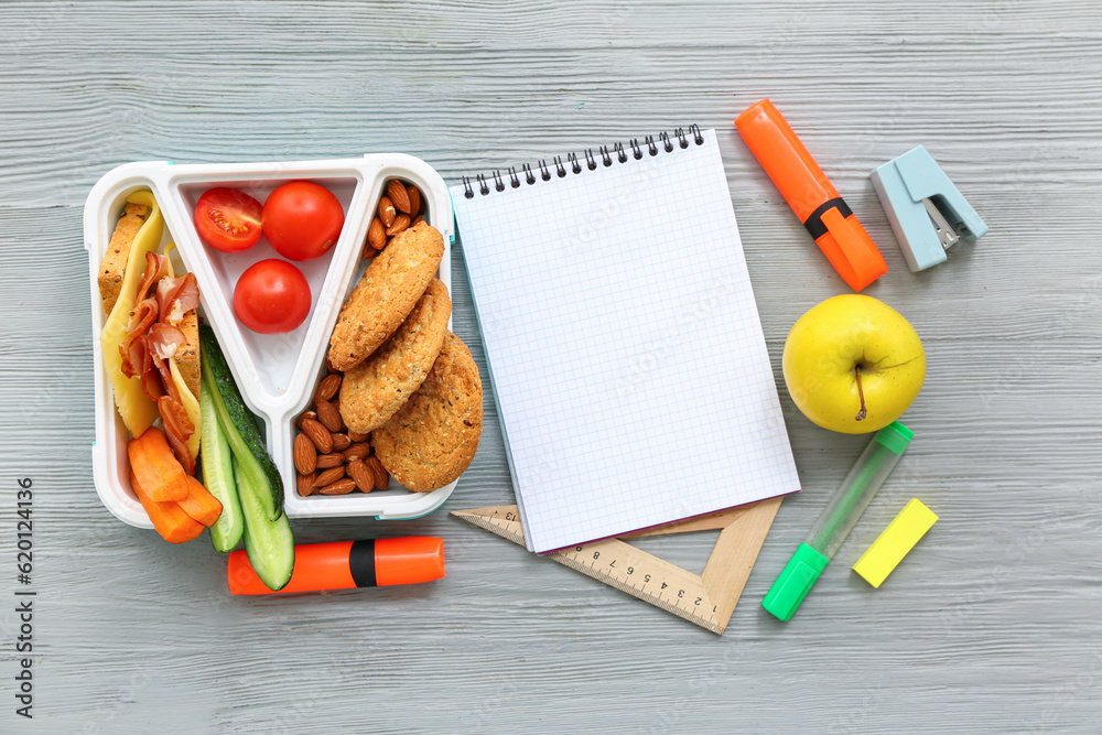 Blank notebook, stationery and lunch box with tasty food on grey wooden background