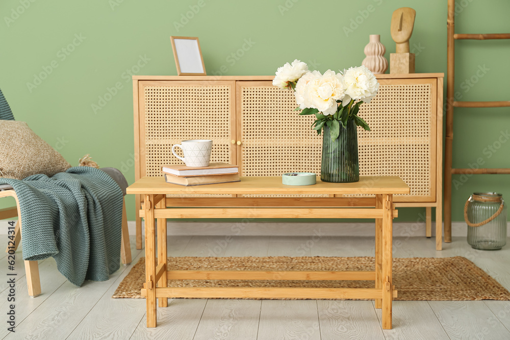 Vase of white peonies on coffee table, chair and dresser near green wall