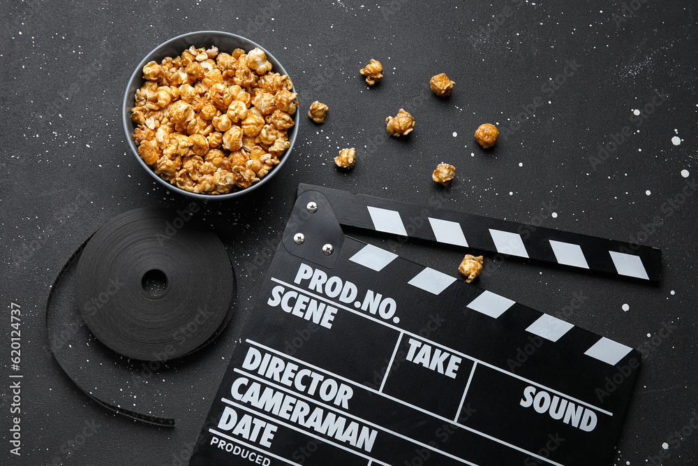 Bowl with tasty popcorn, clapperboard and film reel on black background