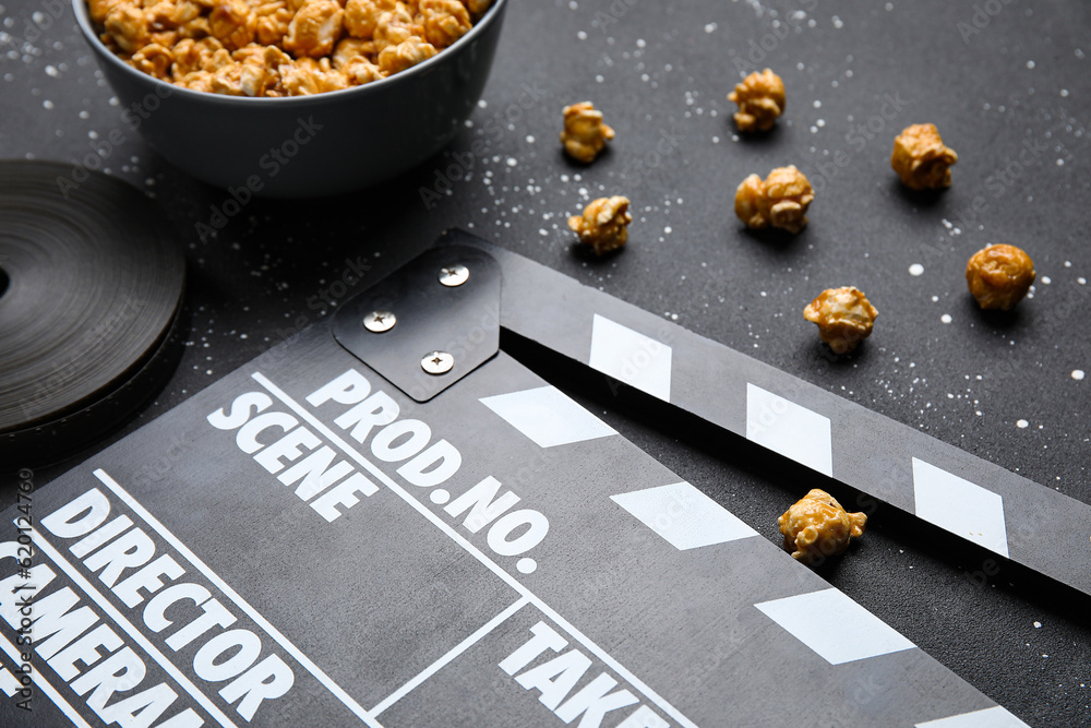 Bowl with tasty popcorn, clapperboard and film reel on black background