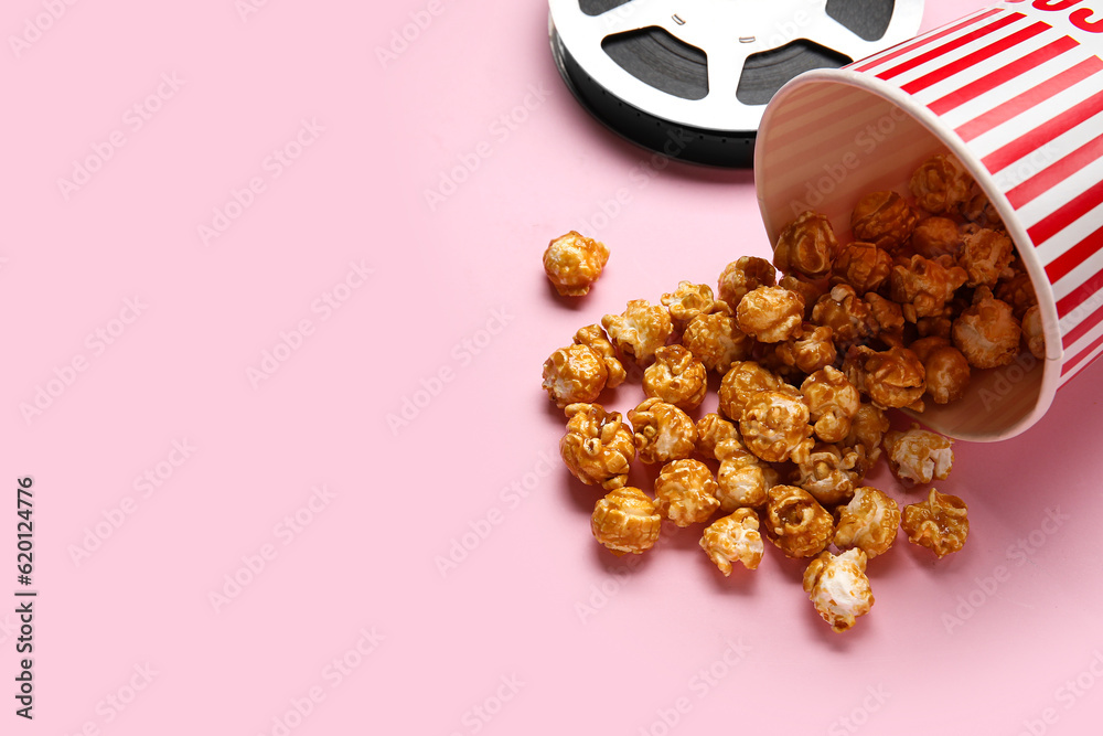 Bucket with tasty popcorn and film reel on pink background