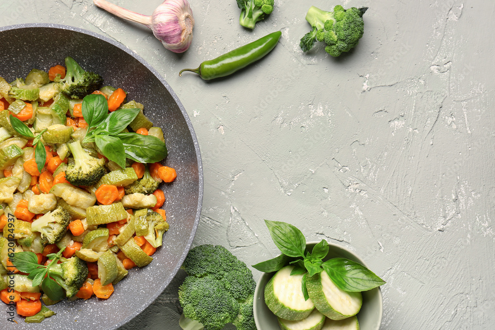 Frying pan with different vegetables on light background