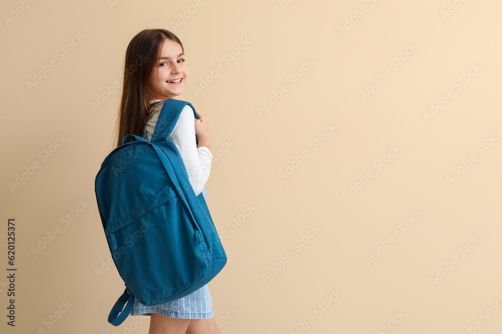 Little schoolgirl with backpack on beige background