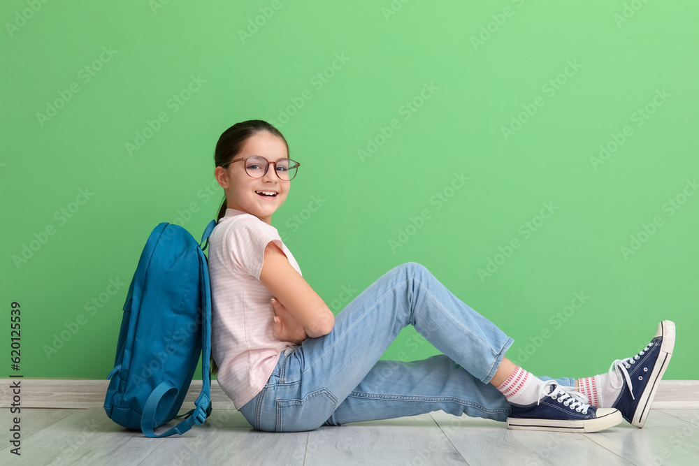 Little girl with backpack near green wall