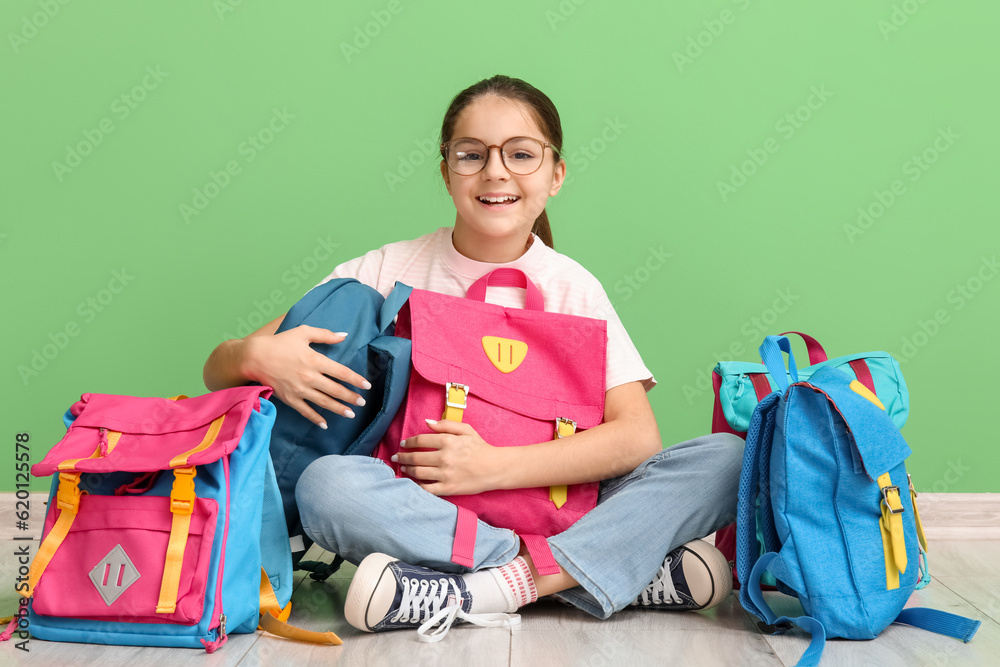 Little girl with backpacks sitting near green wall