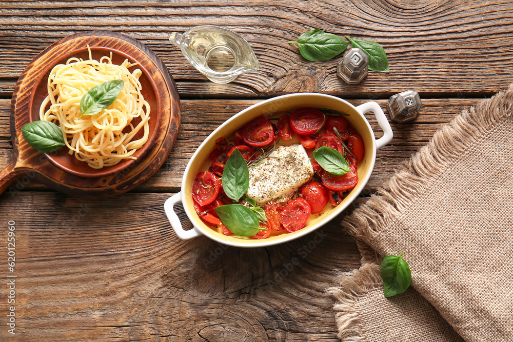 Baking dish with tasty tomatoes, feta cheese and pasta on wooden background