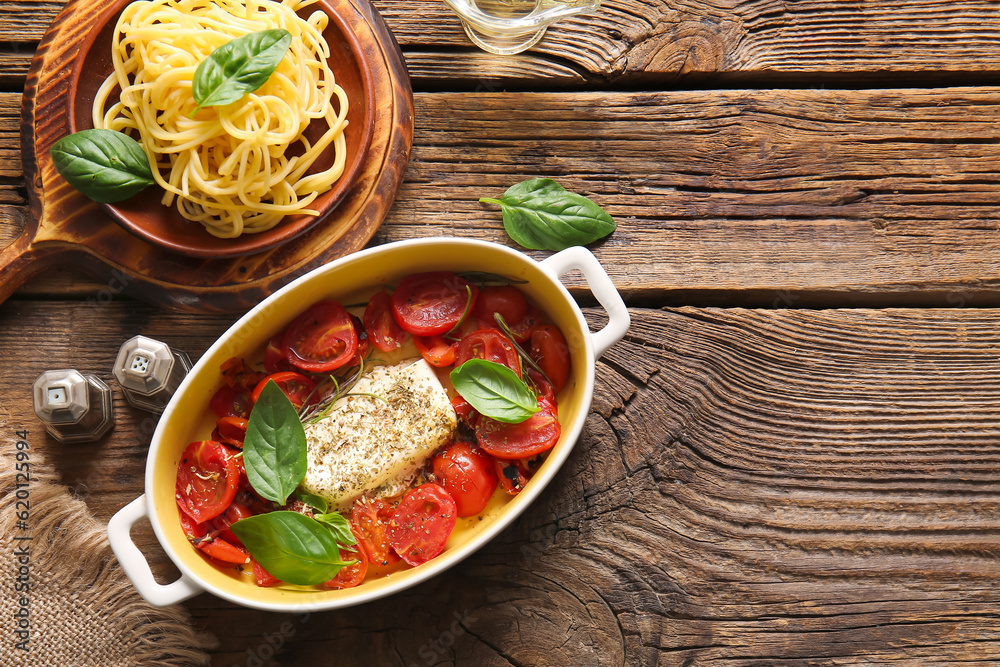 Baking dish with tasty tomatoes, feta cheese and pasta on wooden background